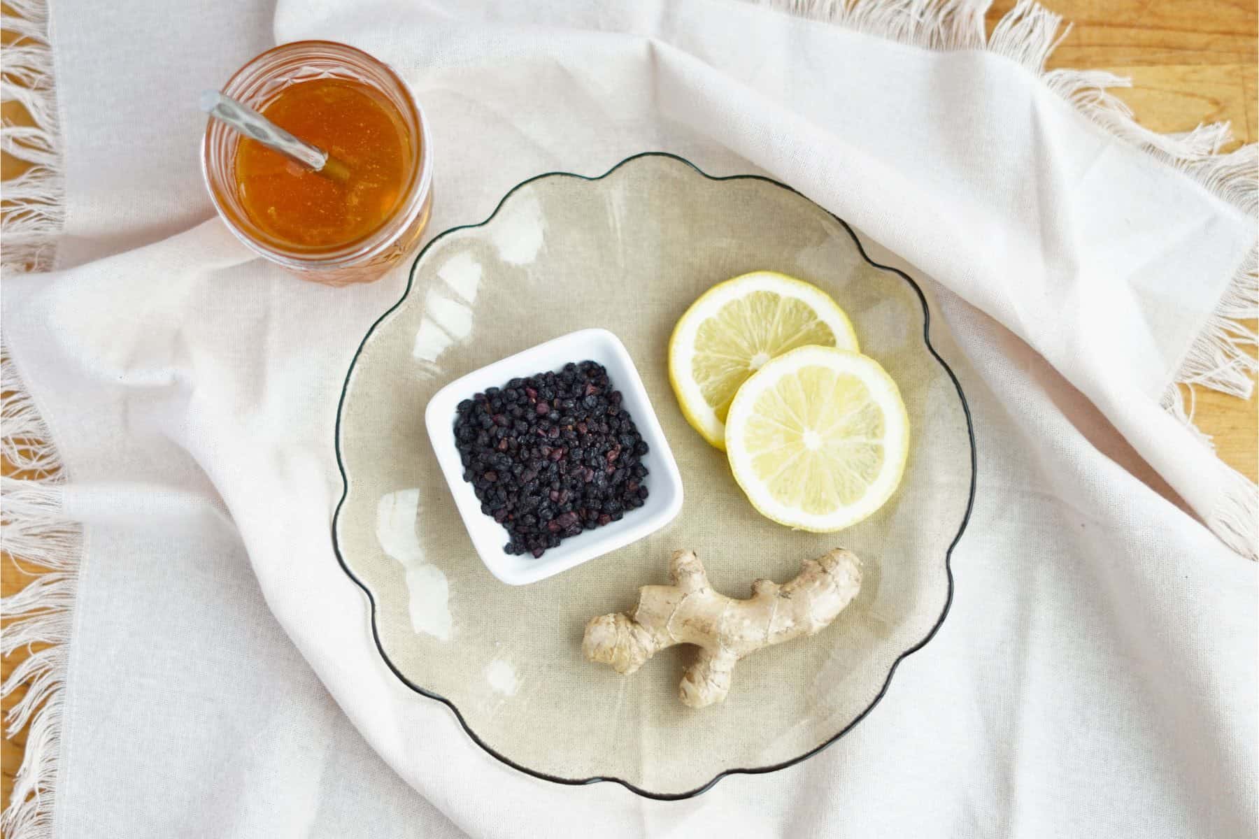 dried elderberries, lemon, and ginger on a plate next to a jar of honey