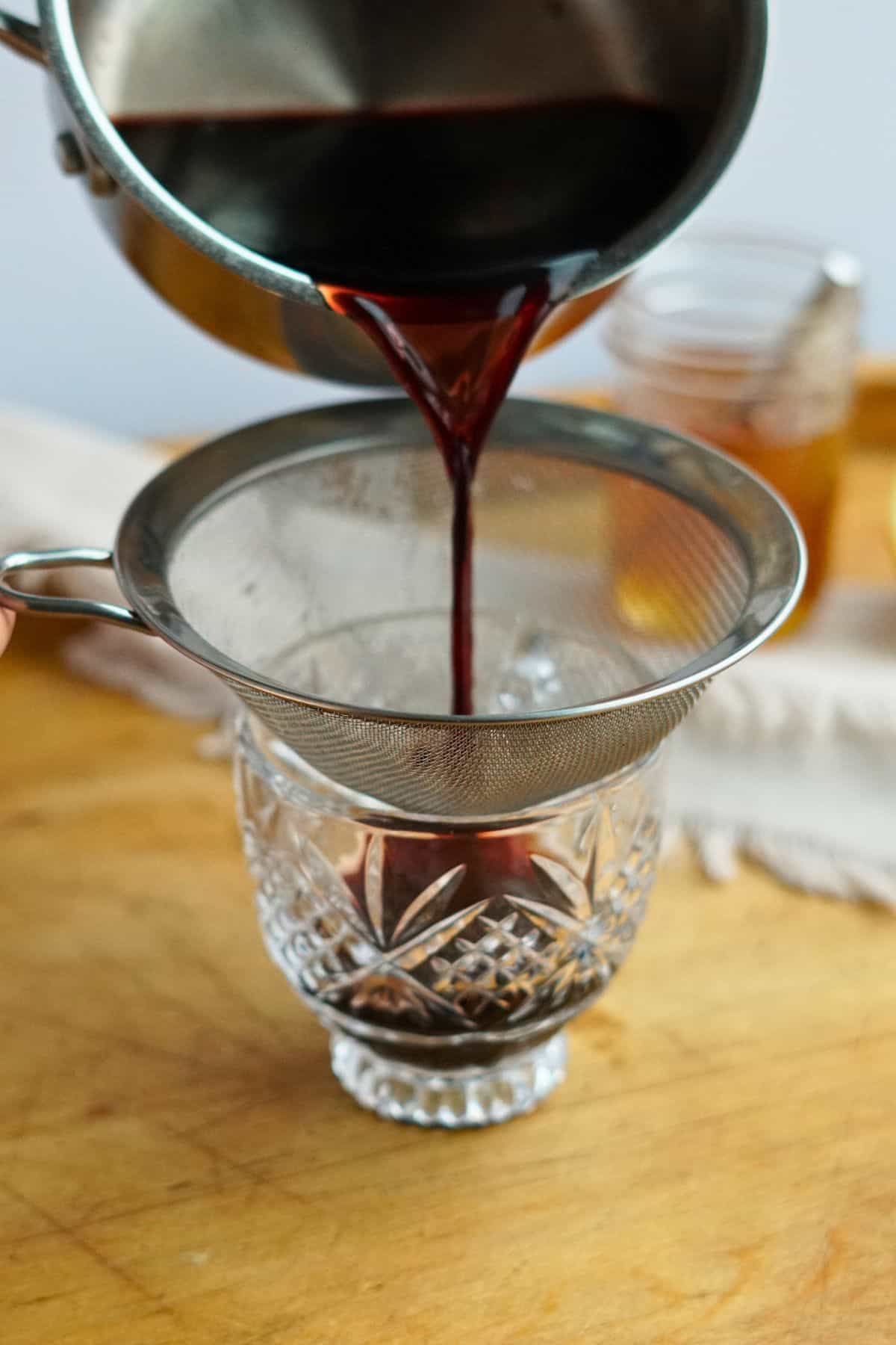 elderberry tea pouring through a sieve into a glass mug