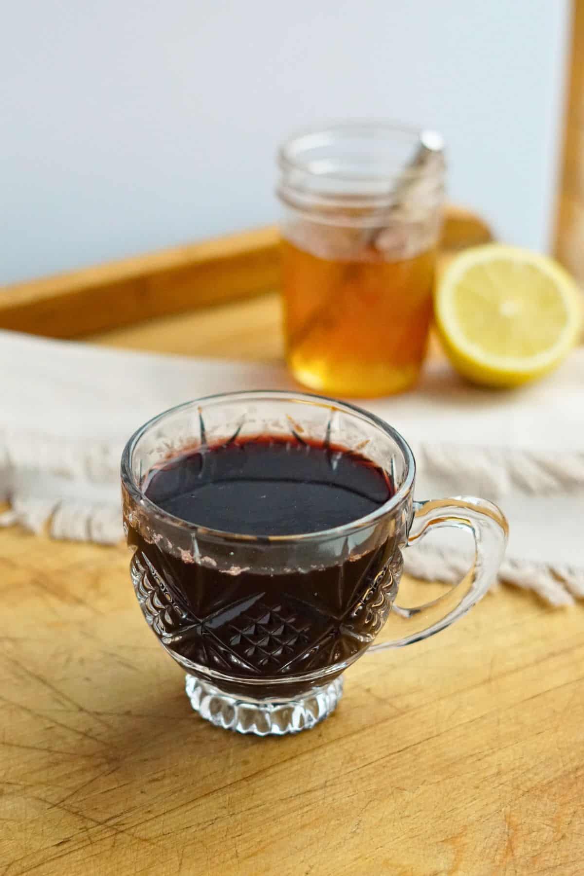 elderberry tea in a glass mug with lemon and jar of honey in the background