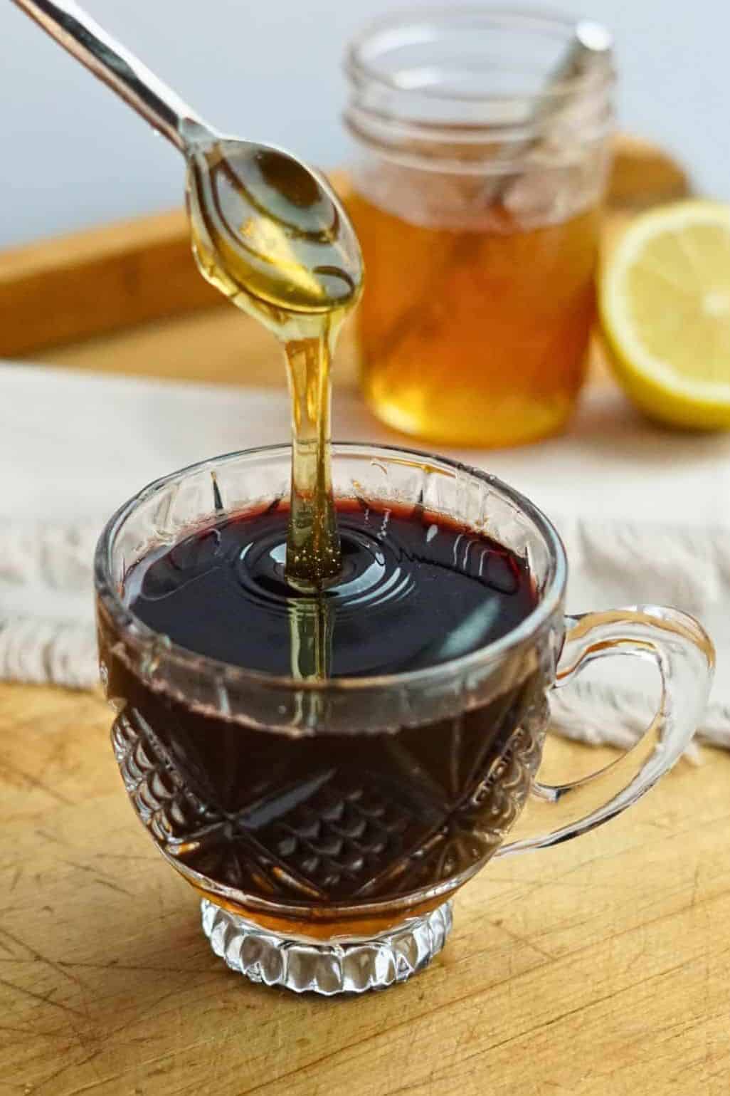 honey pouring into glass mug of elderberry syrup