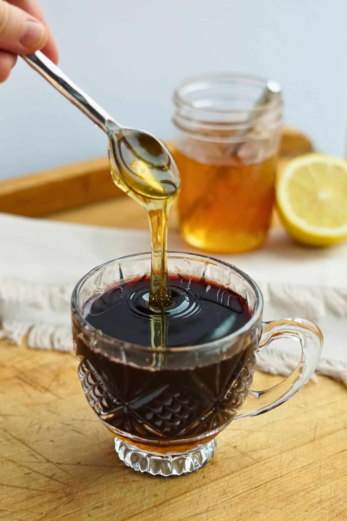 honey pouring into glass mug of elderberry syrup