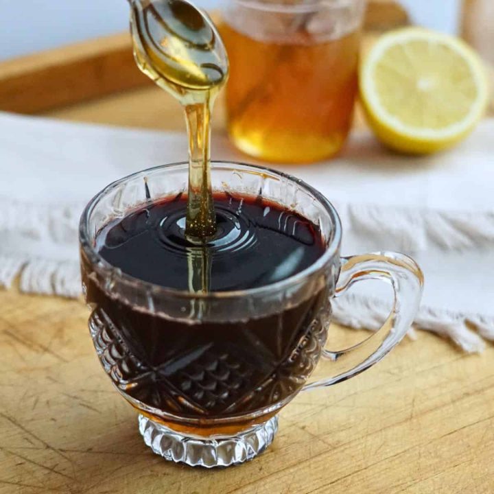 honey pouring into glass of elderberry tea