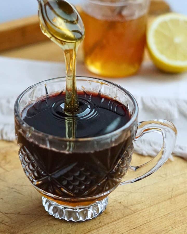 honey pouring into glass of elderberry tea