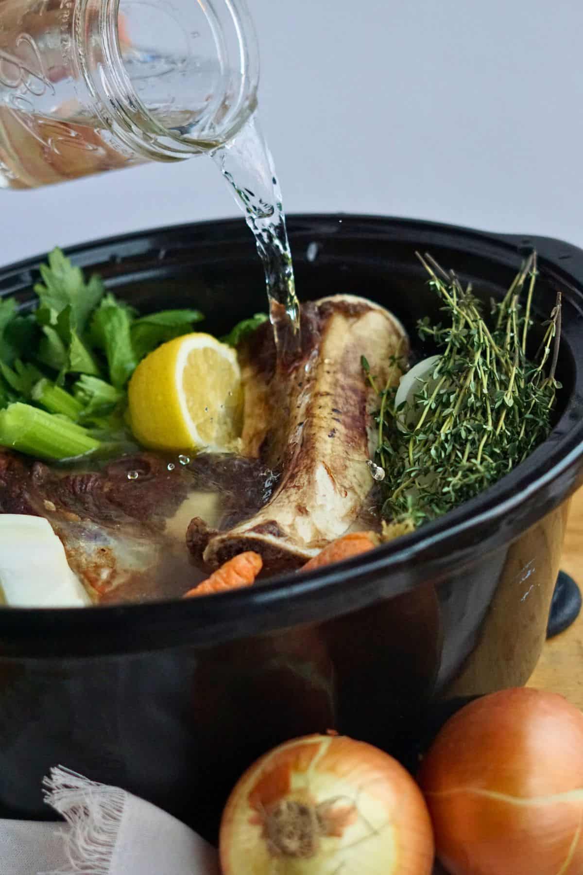 water pouring into crock pot of bones and vegetables