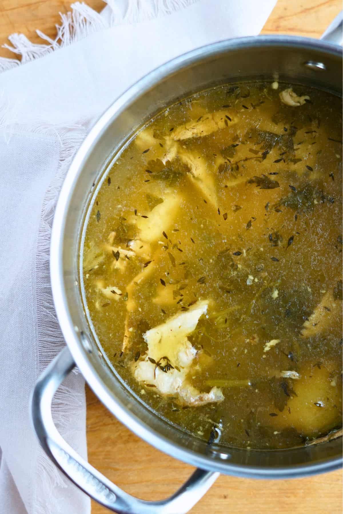 chicken bone broth simmering in pot with herbs