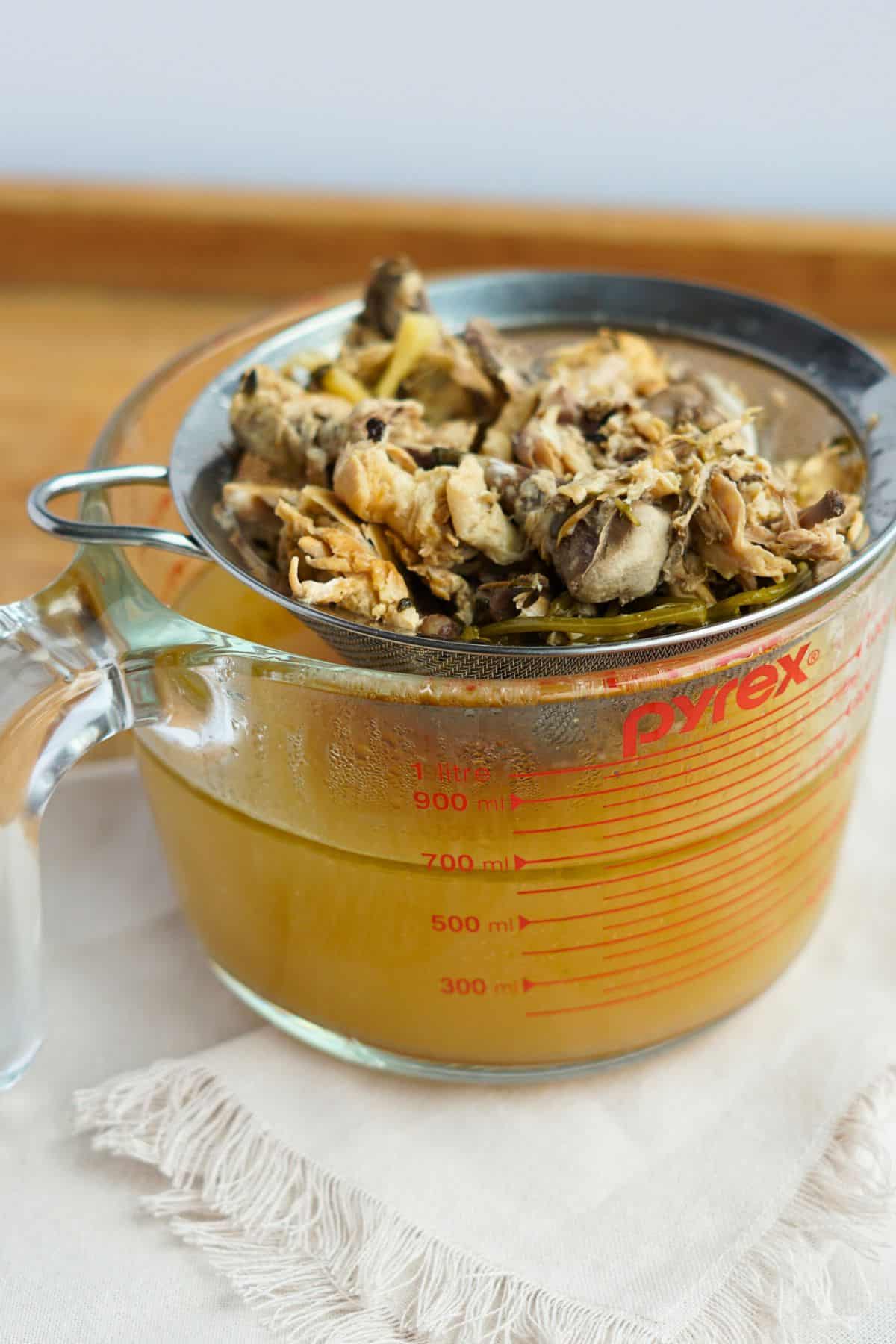 bone broth and bones straining through sieve into glass bowl