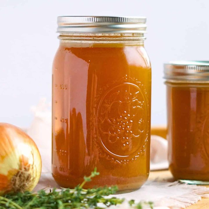 two jars of bone broth on cutting board with onion and herbs