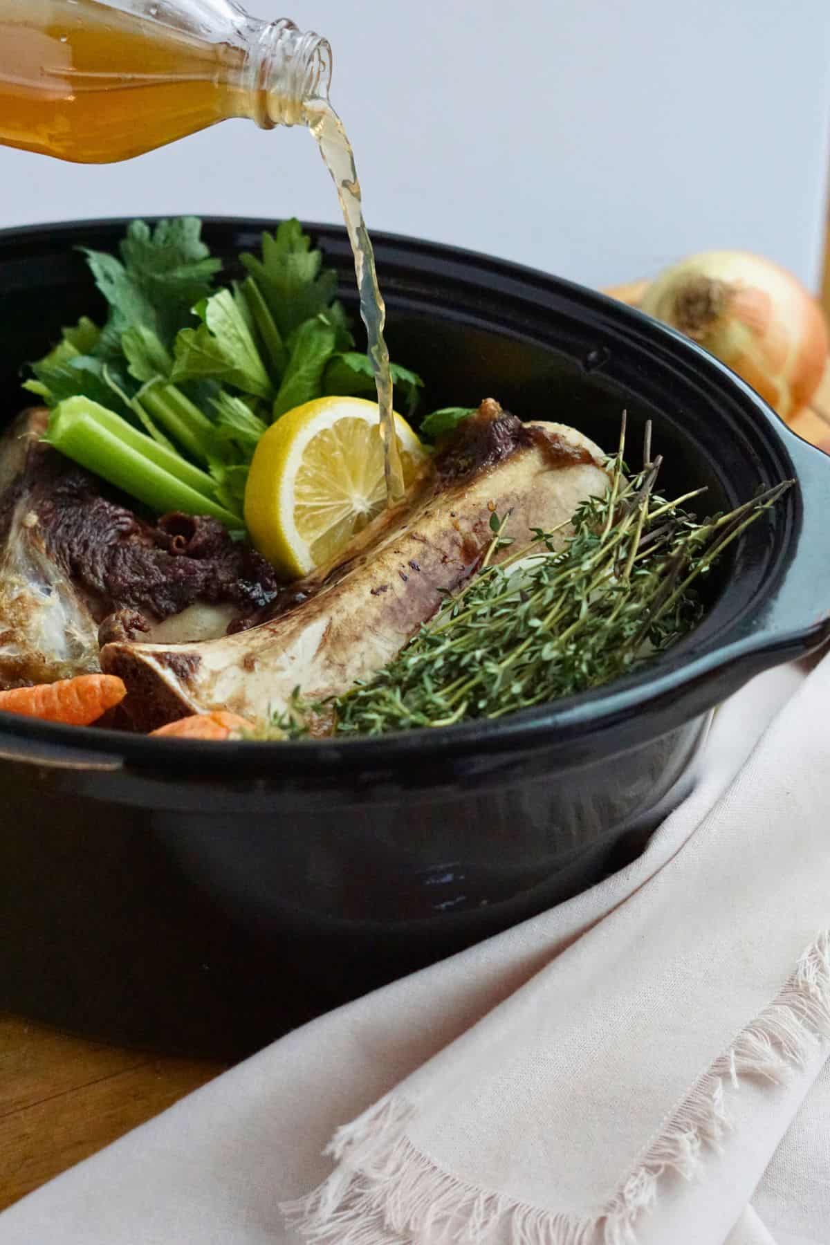 apple cider vinegar pouring into crock pot of bones and vegetables