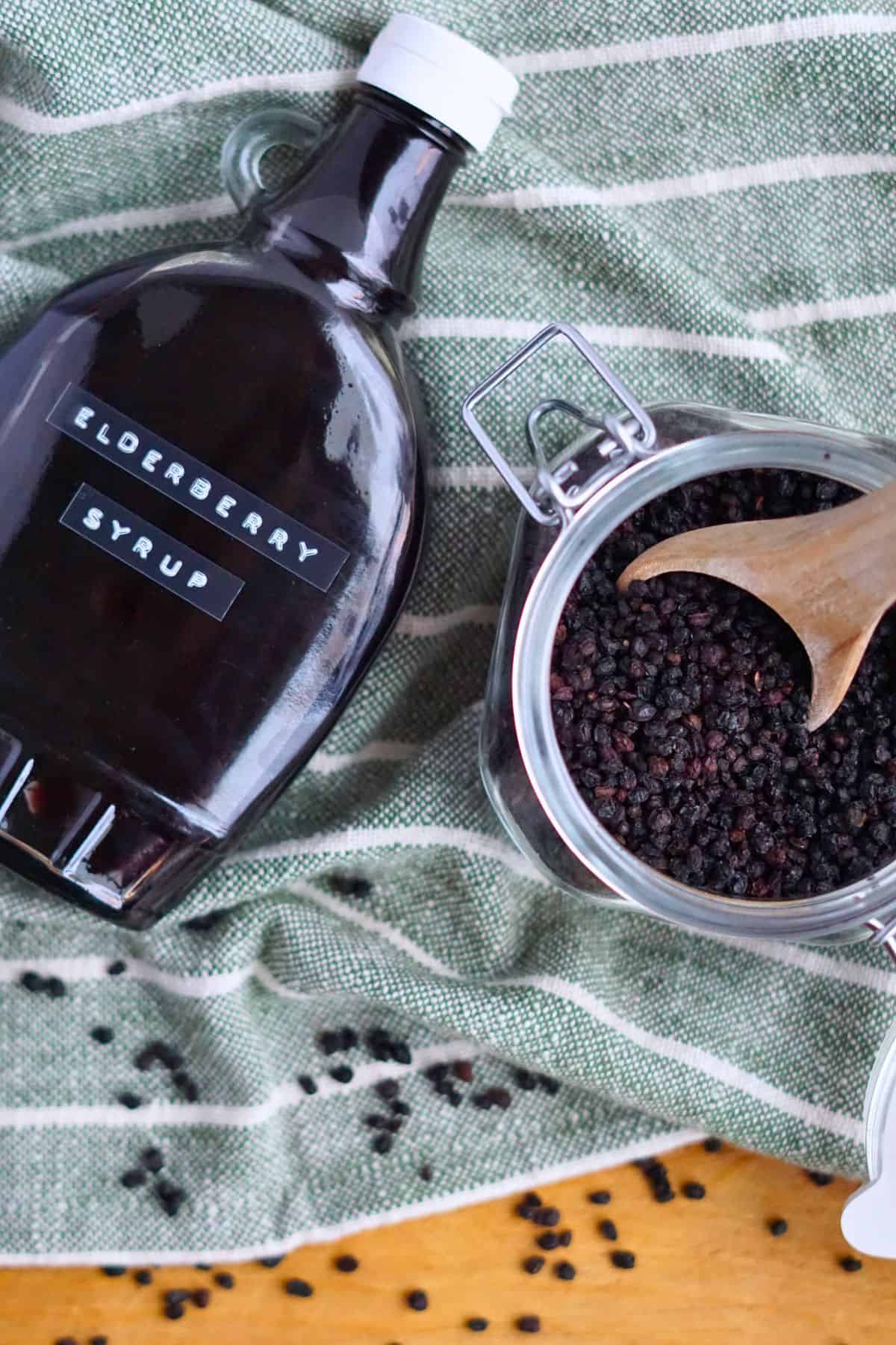 bottle of elderberry syrup on cutting board next to jar of dried elderberries