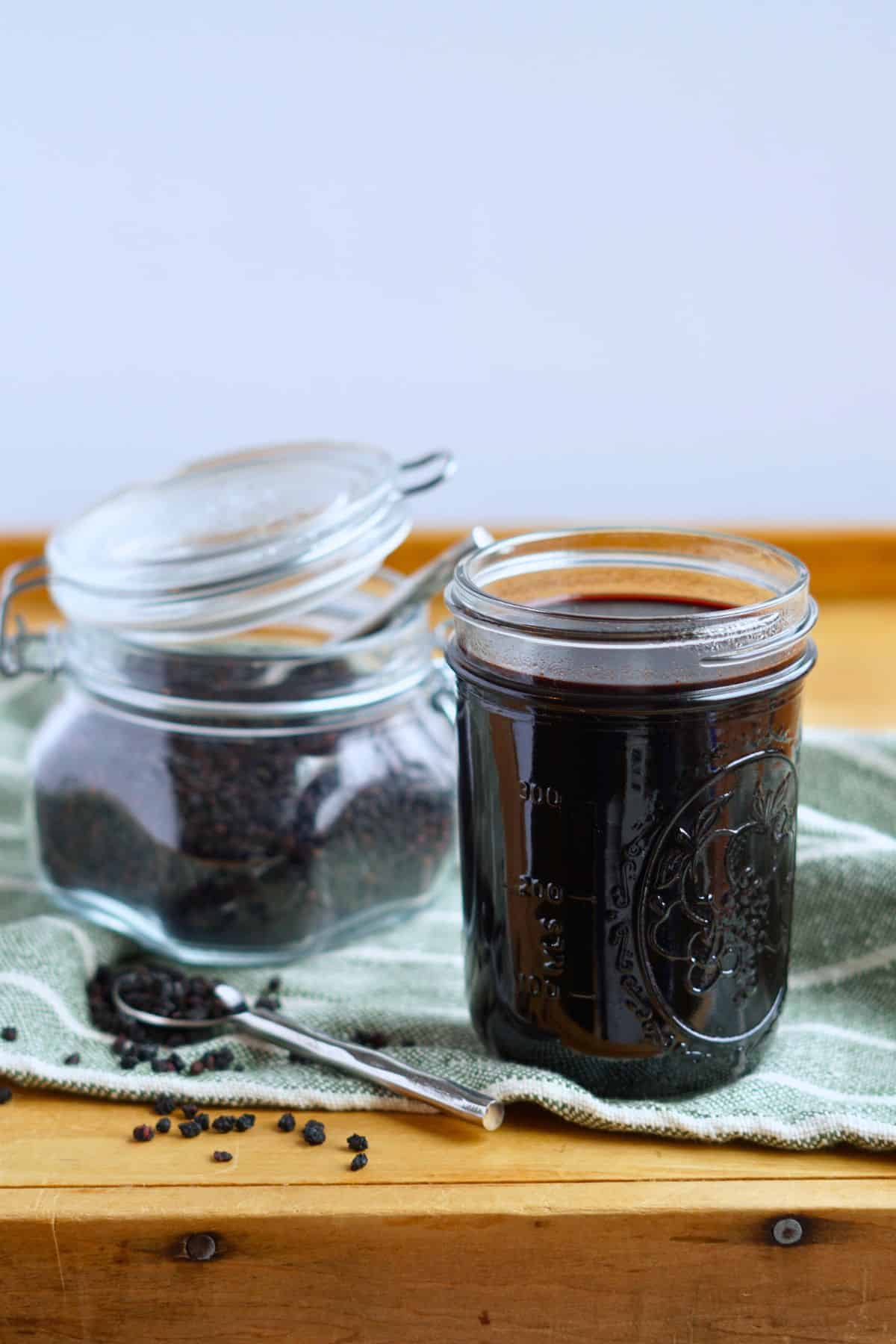 jar of elderberry syrup on cutting board next to jar of dried elderberries