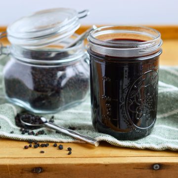 elderberry syrup in a jar with container of dried elderberries in background