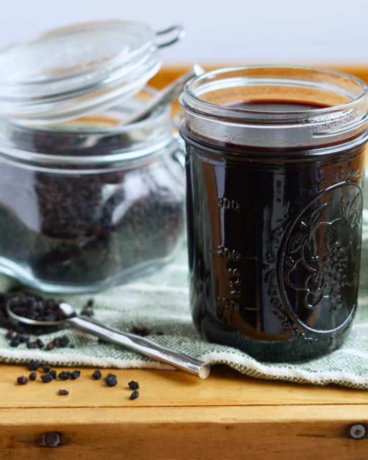 elderberry syrup in a jar with container of dried elderberries in background