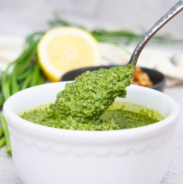 spoon scooping pesto out of white bowl.