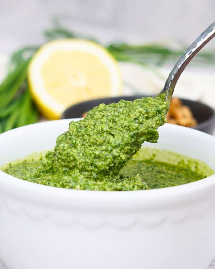 spoon scooping pesto out of white bowl.