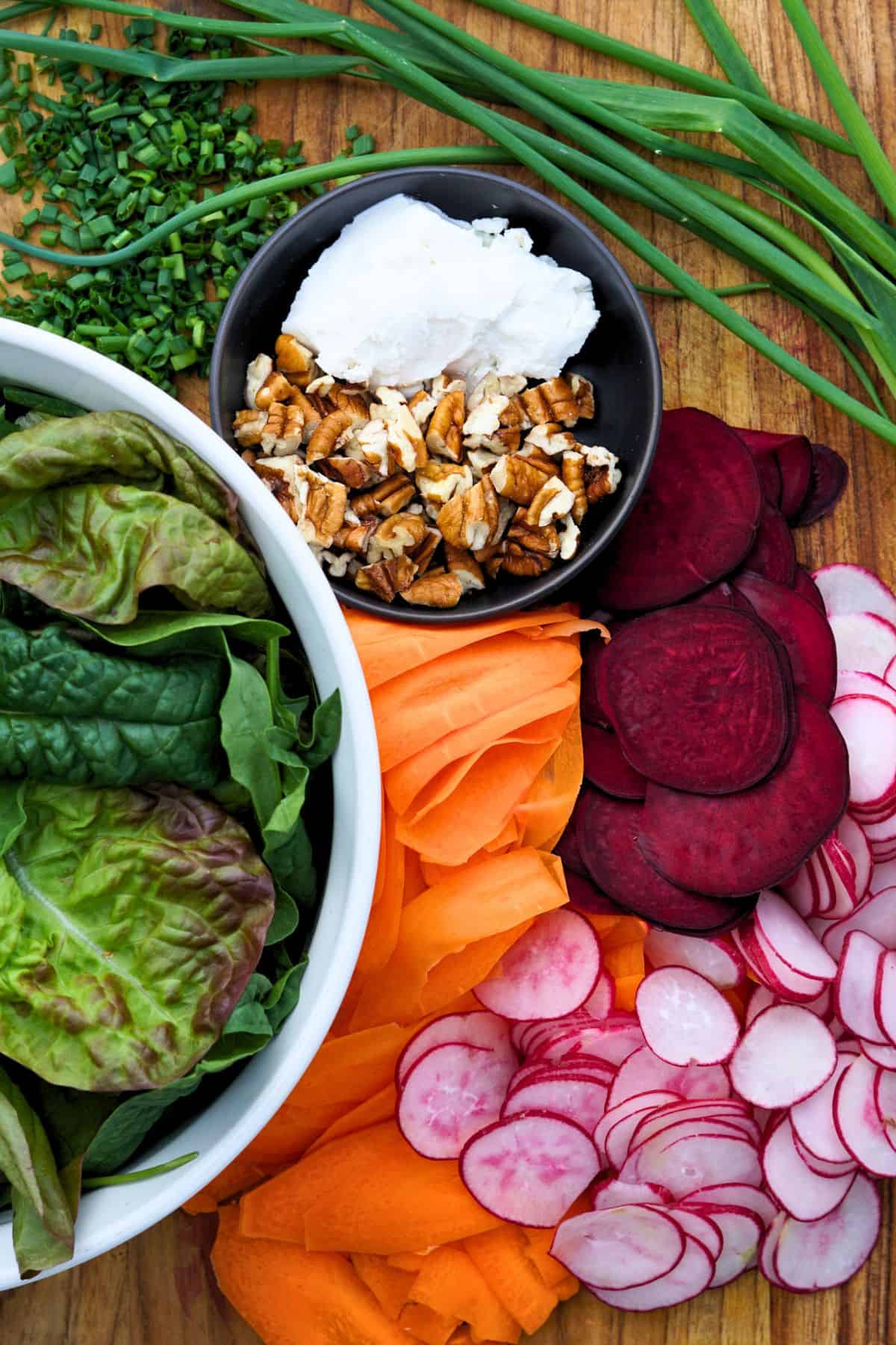 bowl of lettuce next to sliced vegetables on a cutting board