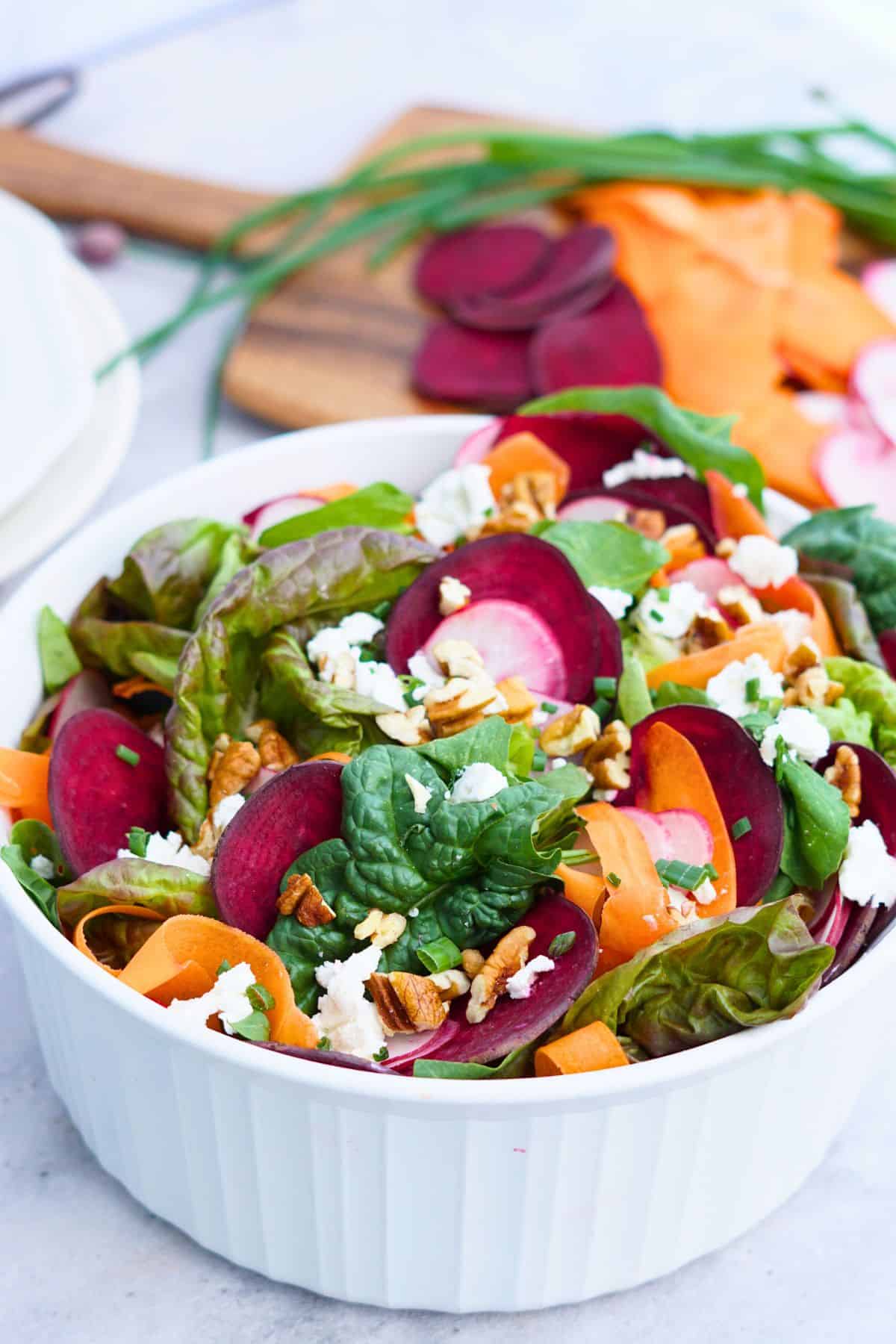 spring salad in a white bowl with sliced vegetables in the background