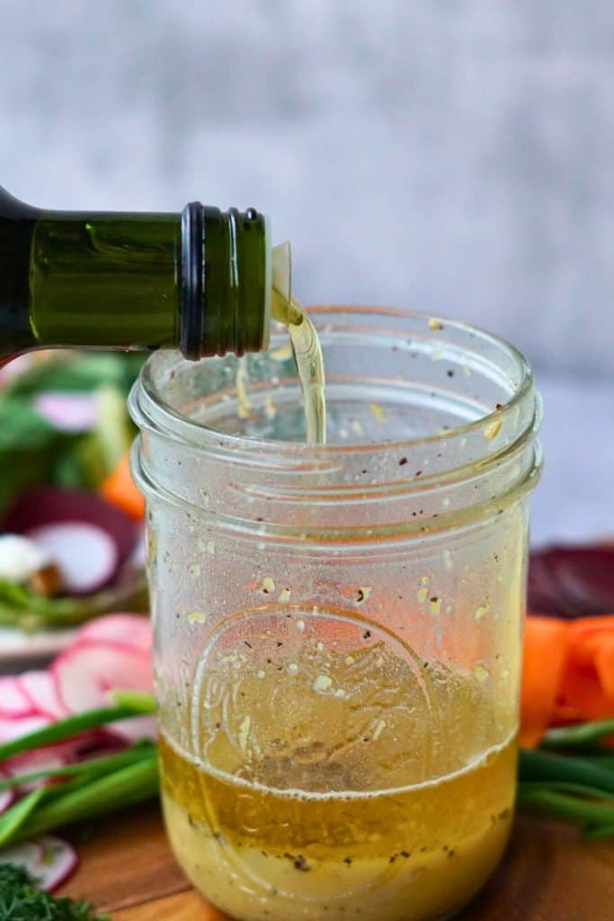 oil pouring into glass container of salad dressing