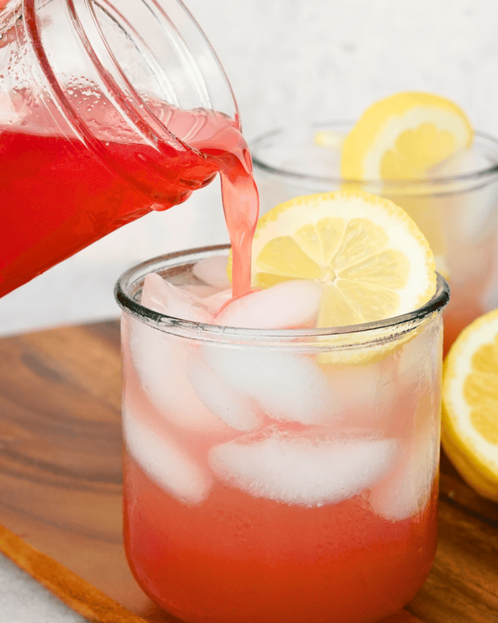 hand pouring simple syrup into glass of ice water