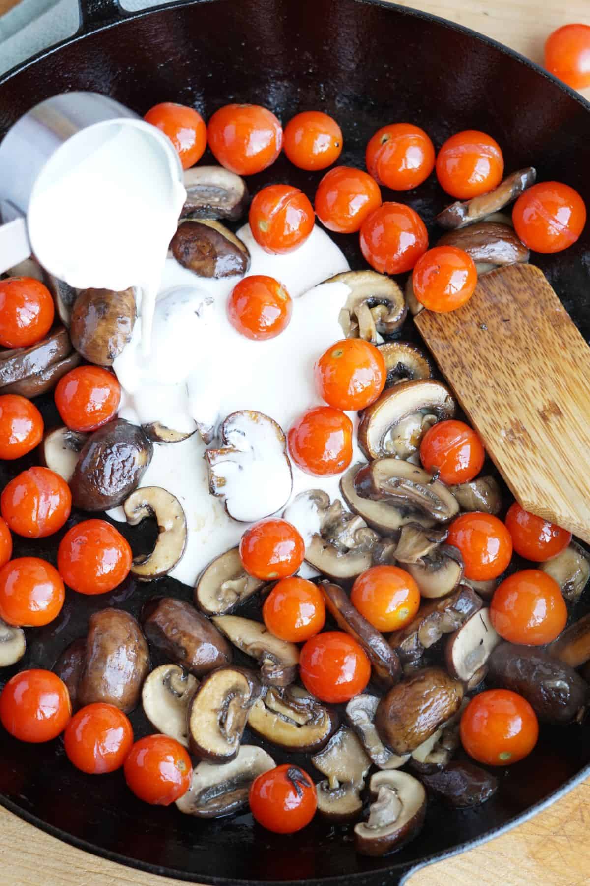 cream pouring into cast iron pan of sauteed mushrooms and tomatoes
