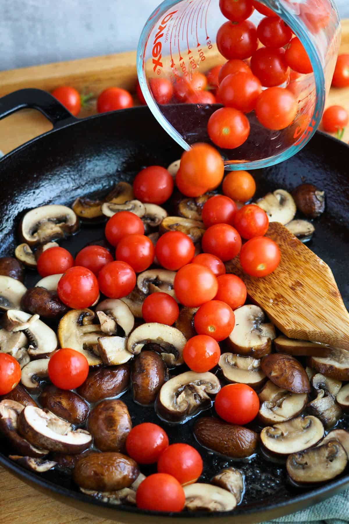 cherry tomatoes pouring into cast iron pan with sauteed mushrooms
