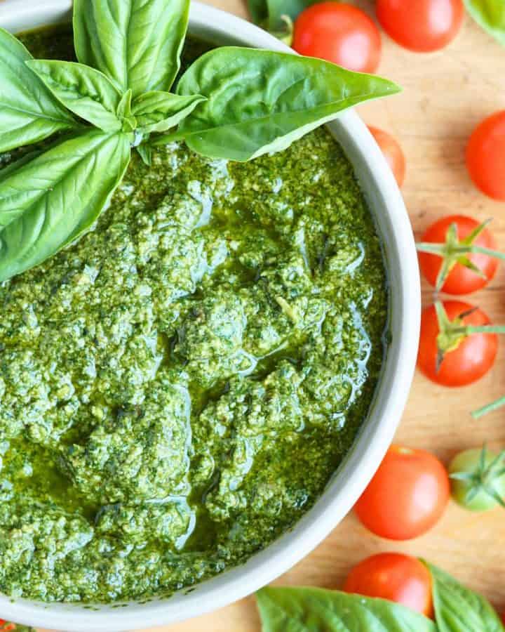 close up of finished pesto in white bowl on wooden cutting board next to cherry tomatoes