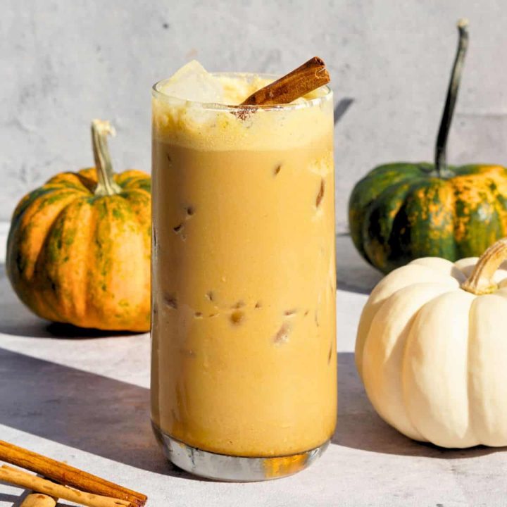 iced bone broth pumpkin spice latte in glass on counter next to cinnamon sticks and mini pumpkins