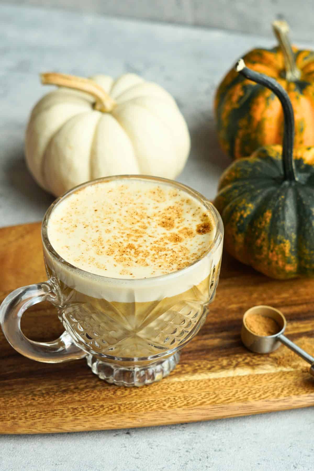 bone broth pumpkin spice latte in glass mug on counter next to small multicolor pumpkins