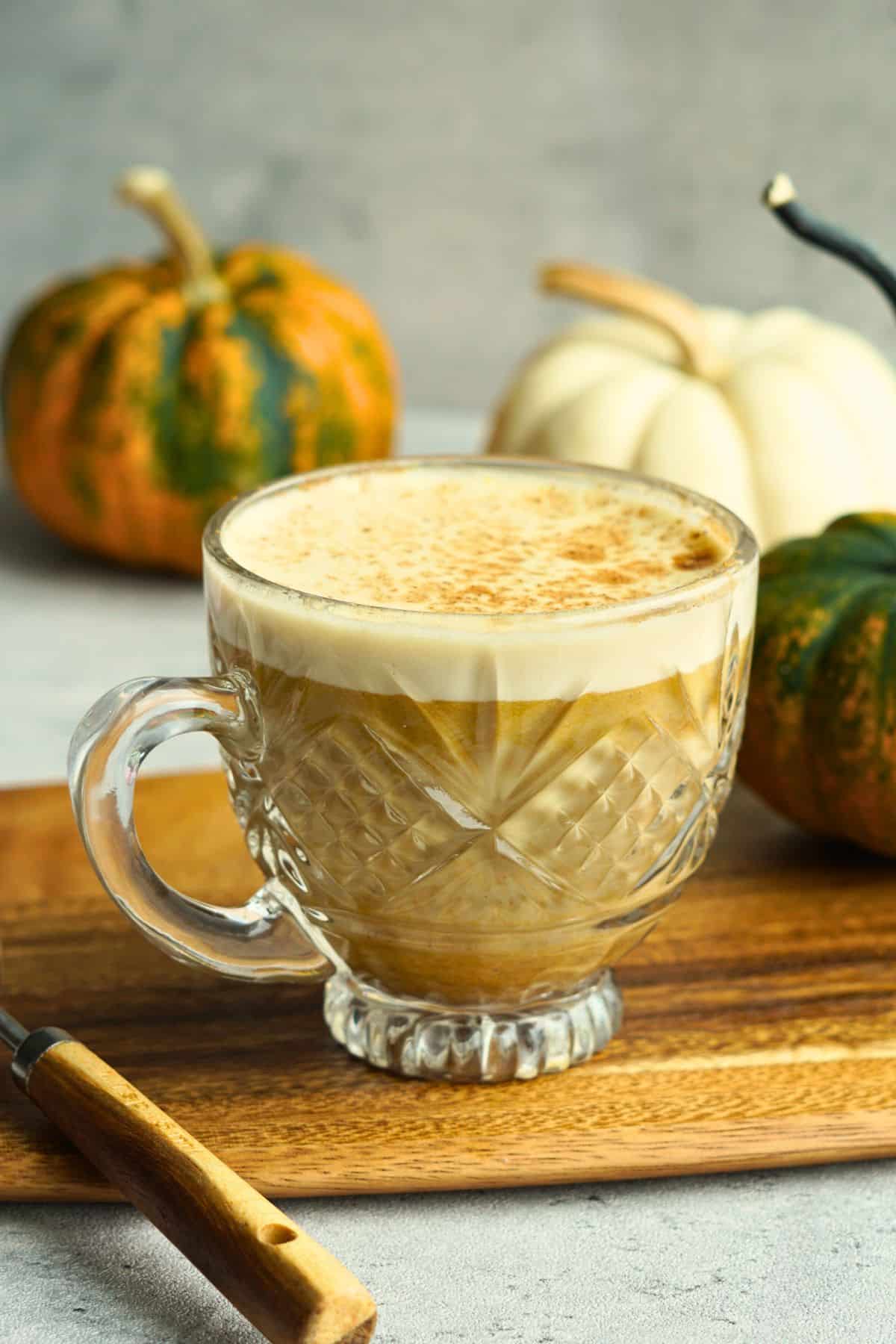 bone broth pumpkin spice latte in glass mug on counter next to small multicolor pumpkins