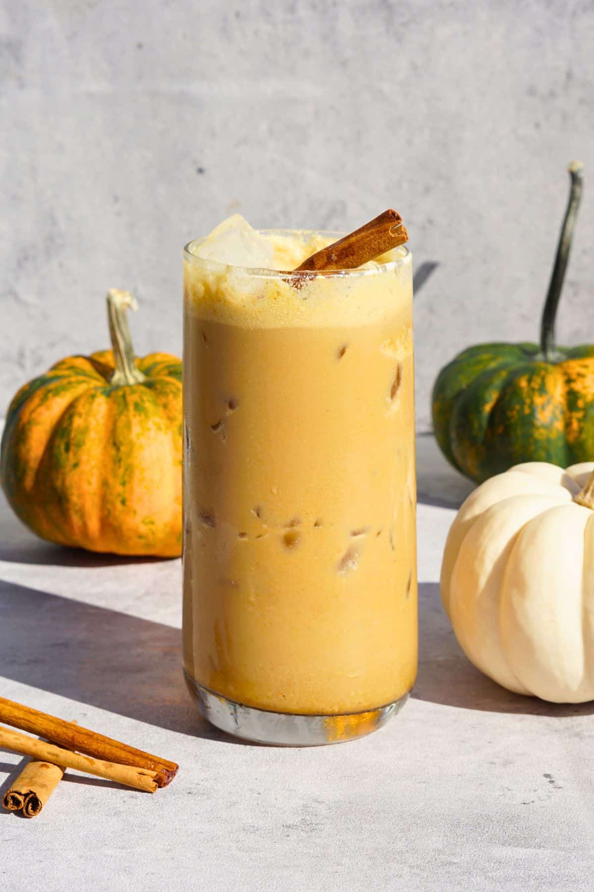 iced bone broth pumpkin spice latte in glass on counter next to cinnamon sticks and mini pumpkins