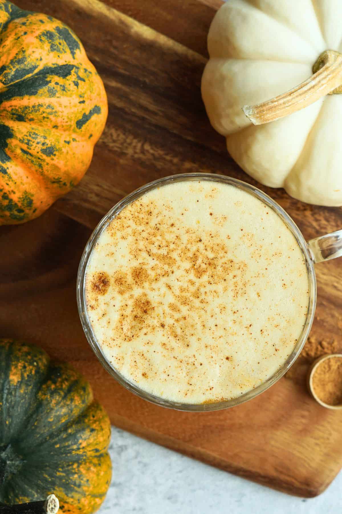 bone broth pumpkin spice latte in glass mug dusted with cinnamon on counter next to small multicolor pumpkins