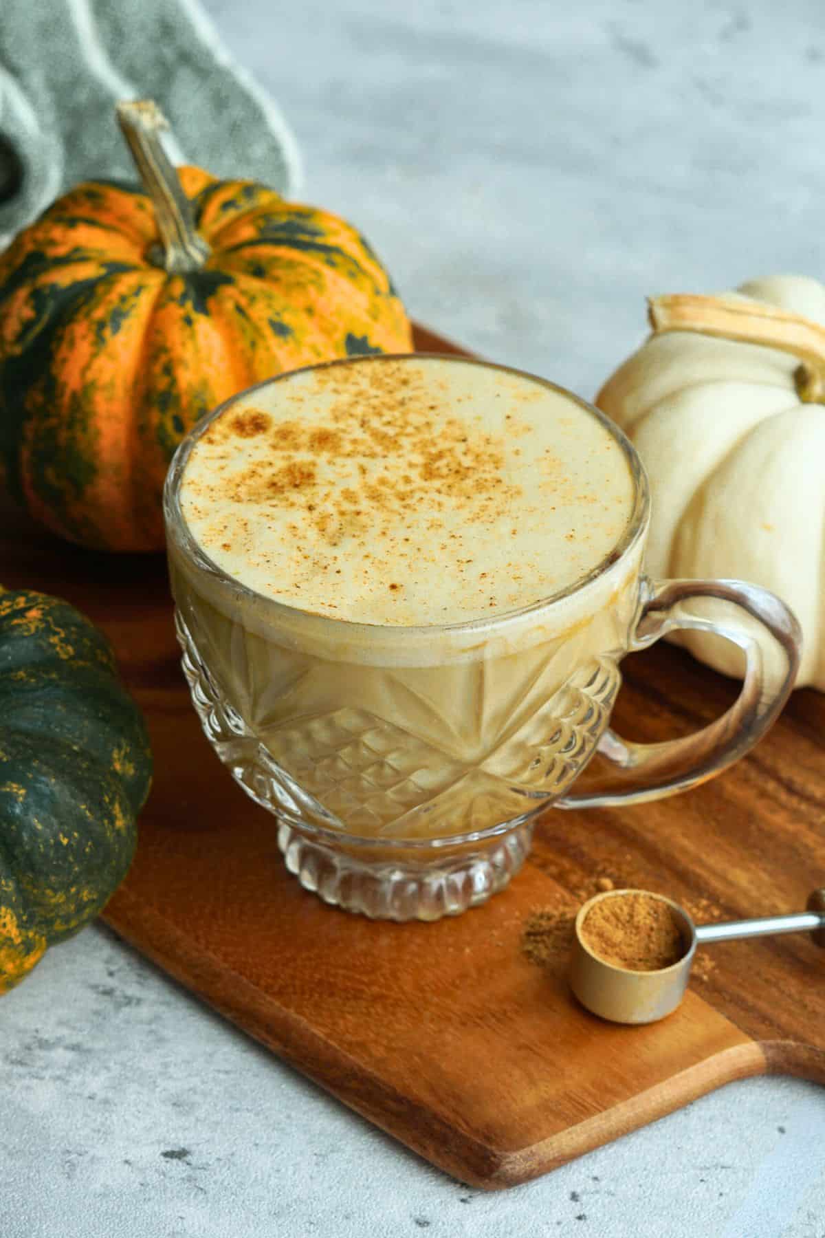 bone broth pumpkin spice latte in glass mug on counter next to small multicolor pumpkins