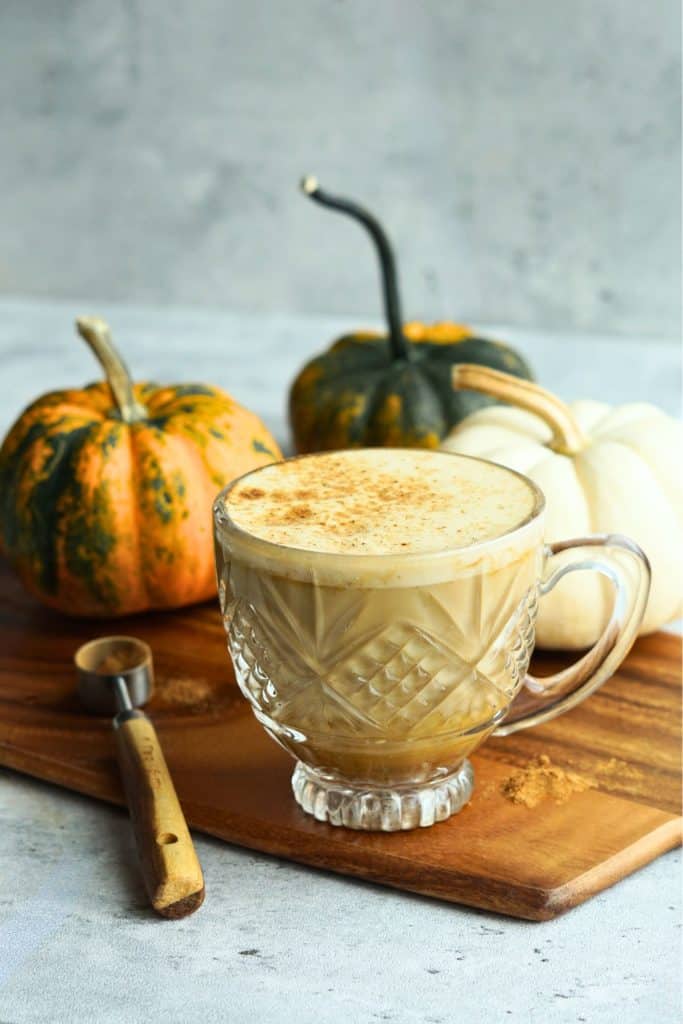bone broth pumpkin spice latte in glass mug on counter next to small multicolor pumpkins