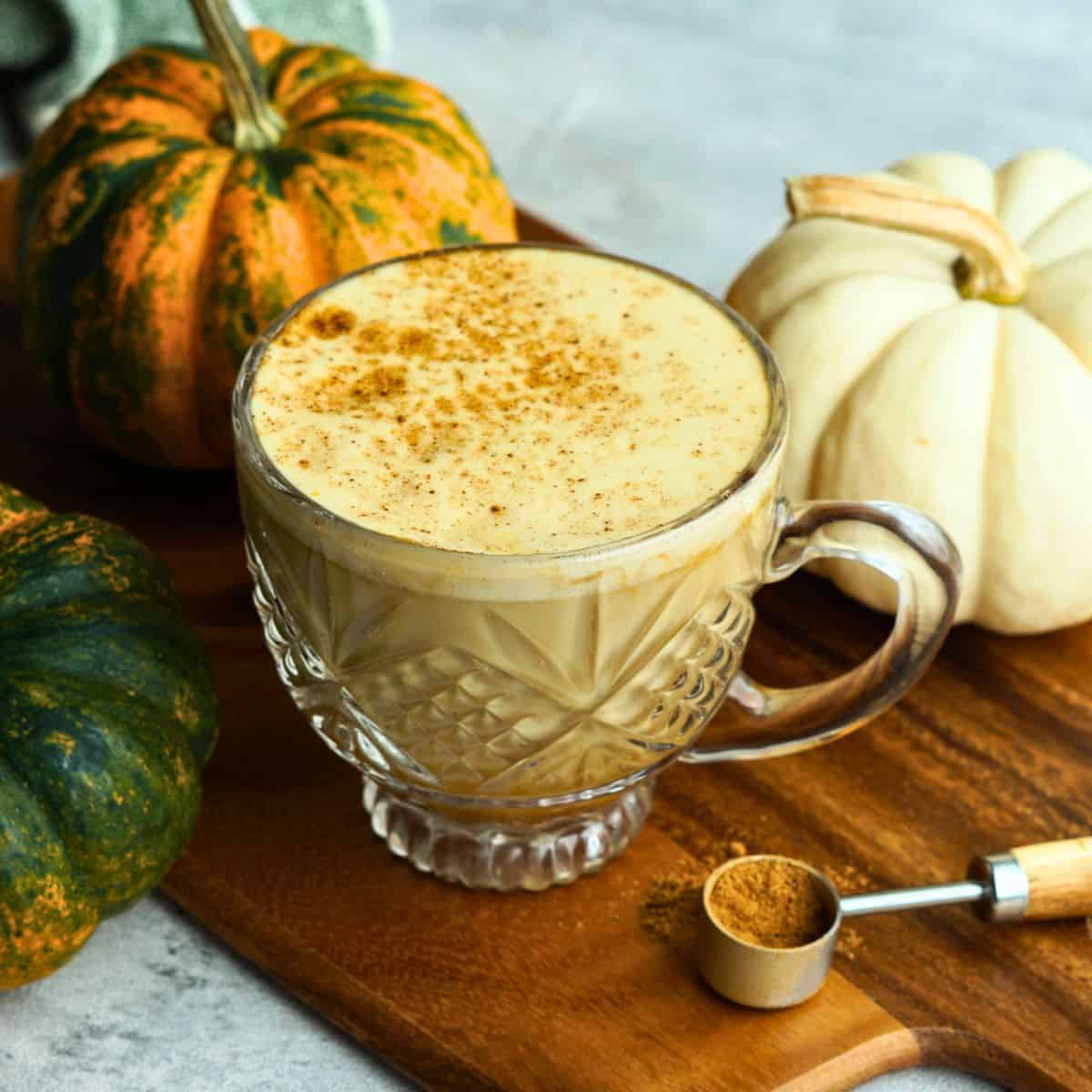 bone broth pumpkin spice latte in glass mug on counter next to small multicolor pumpkins