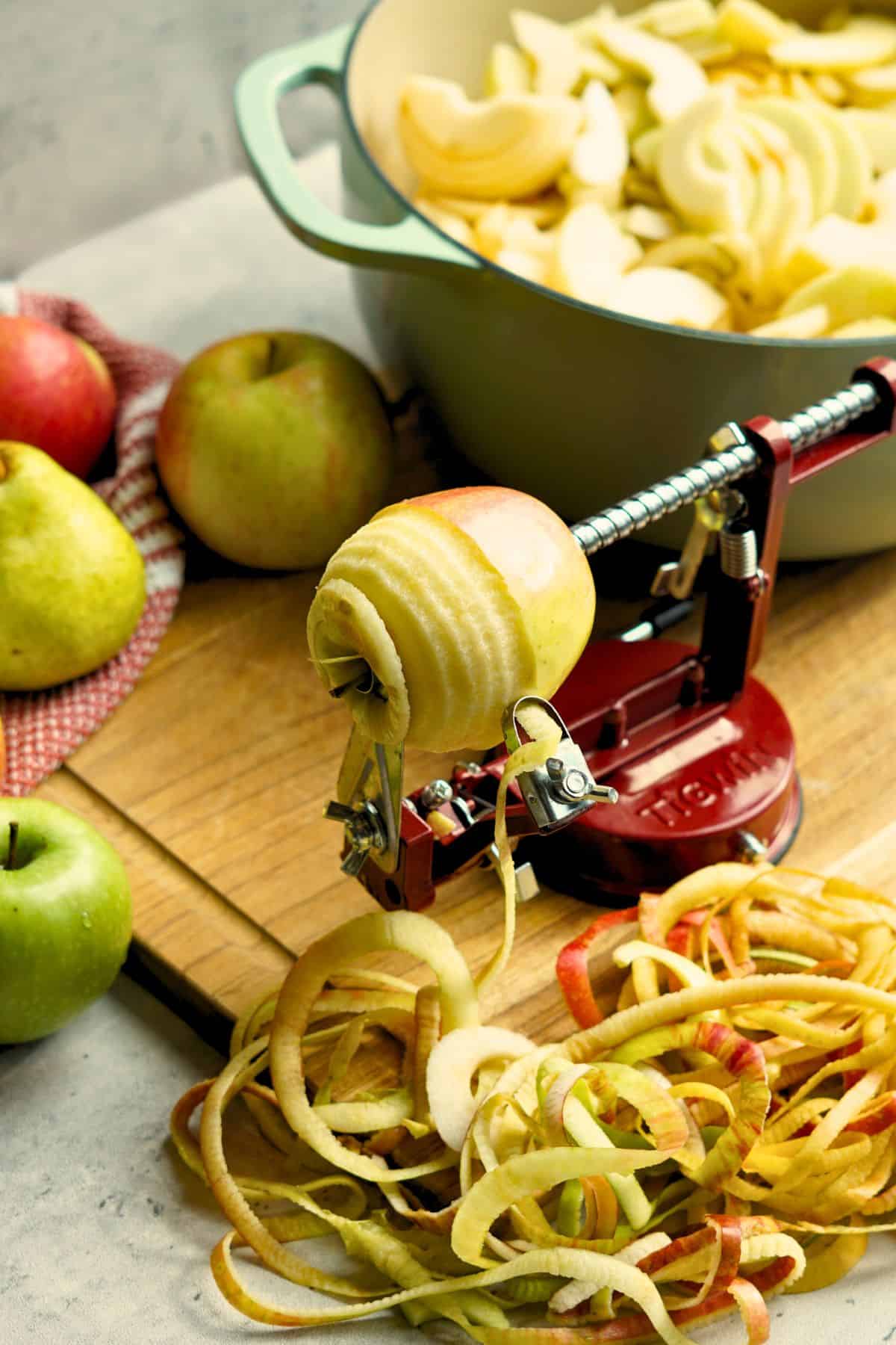 An apple being peeled, sliced, and cored with pot and whole apples in the background
