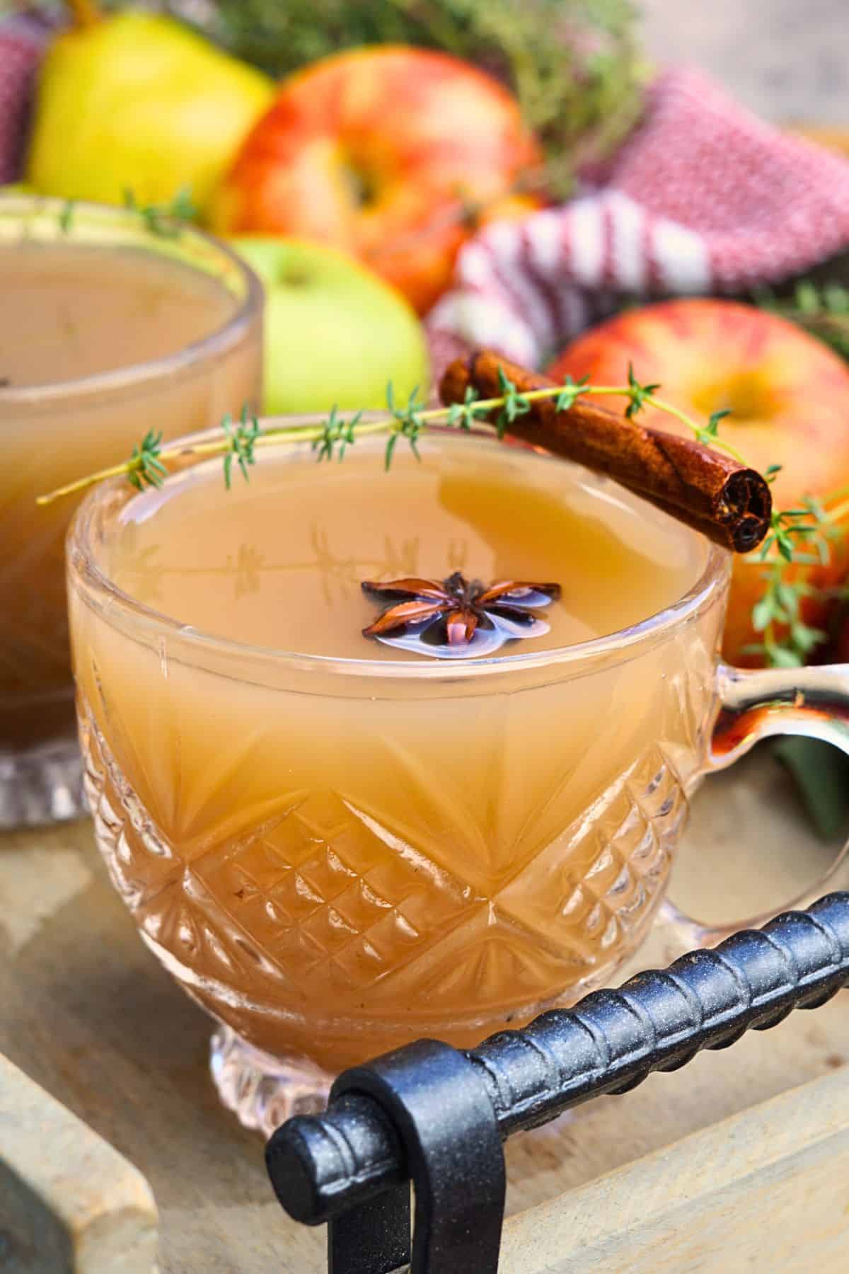 close up of glass of spiced apple scrap cider garnished with cinnamon sticks and star anise on tray