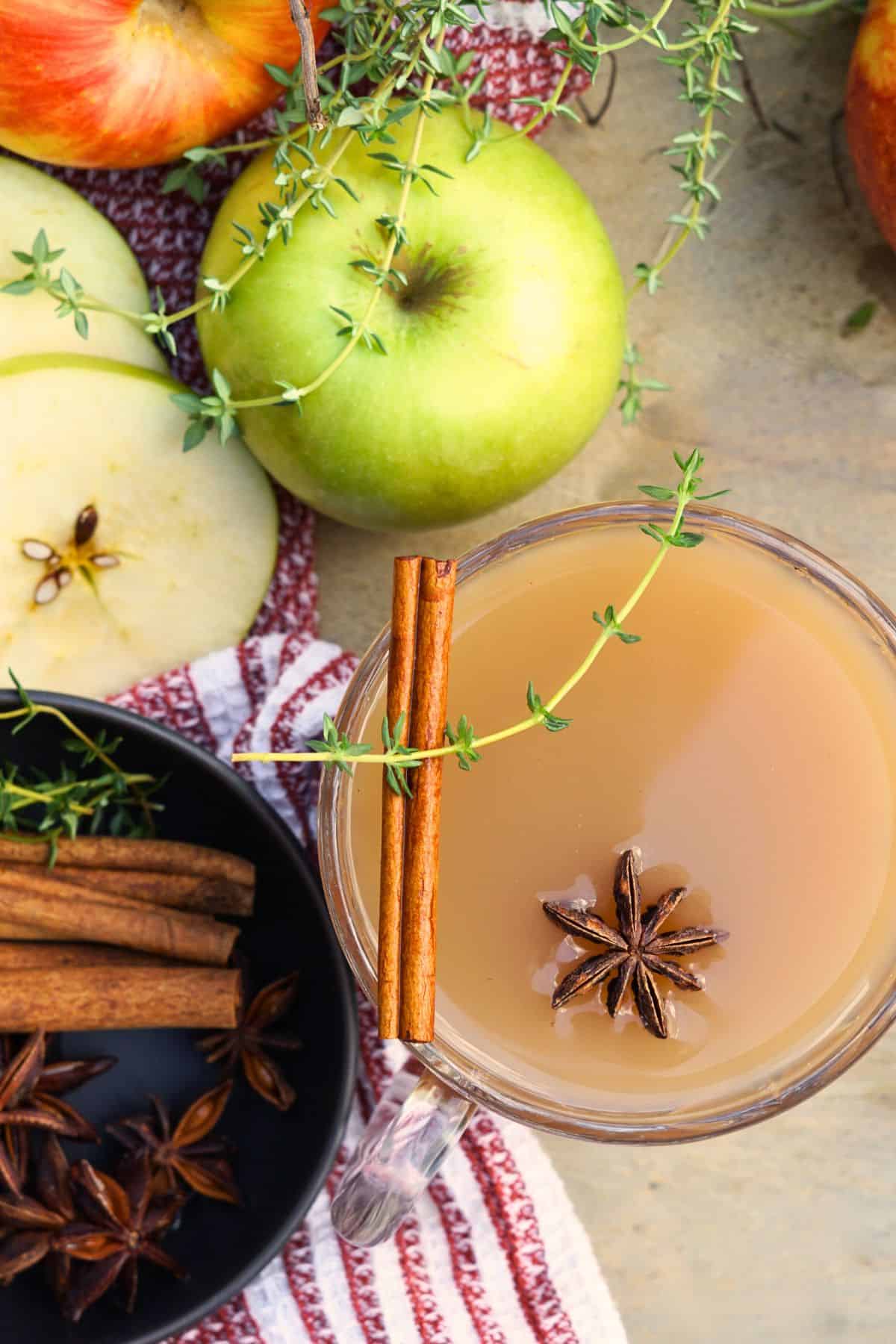 close up of glass of spiced apple scrap cider garnished with cinnamon sticks and star anise on tray next to small bowl of whole spices