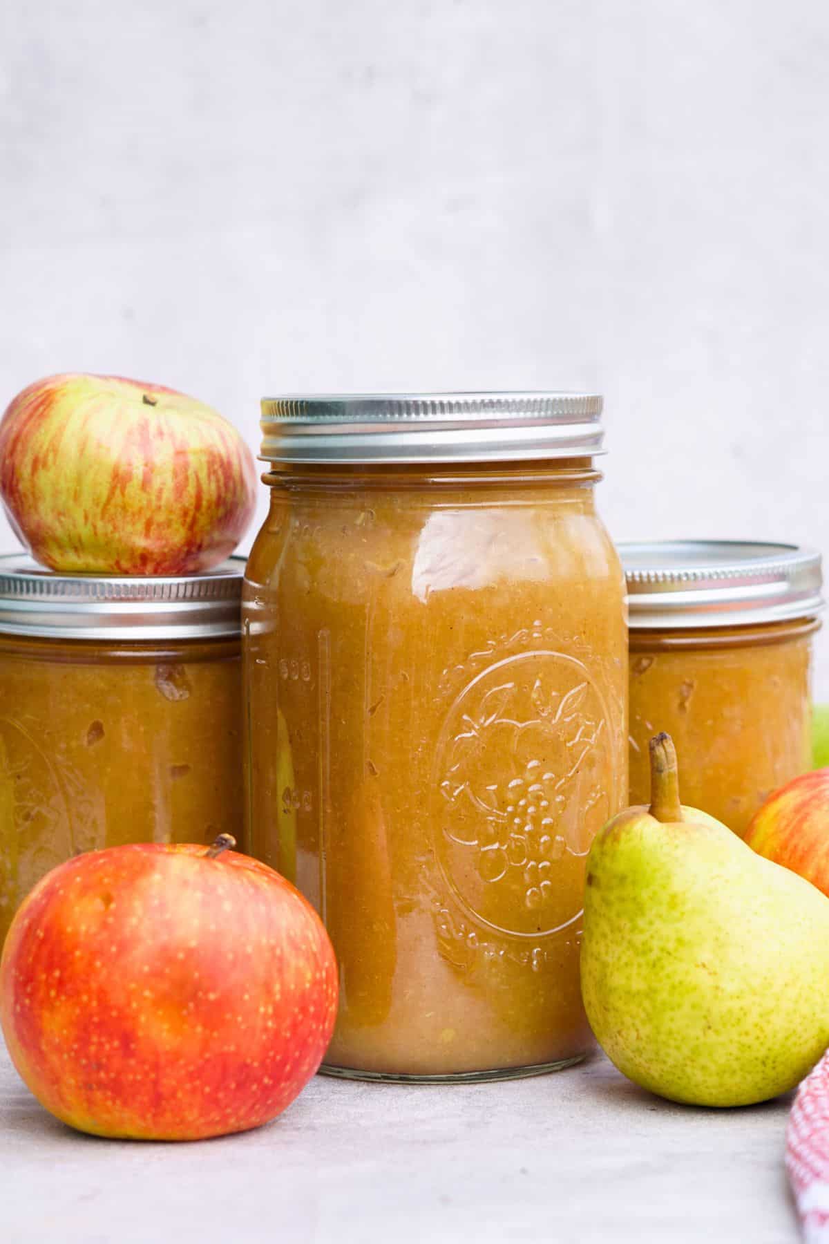 3 jars of spiced pear applesauce on counter next to whole apples and pears