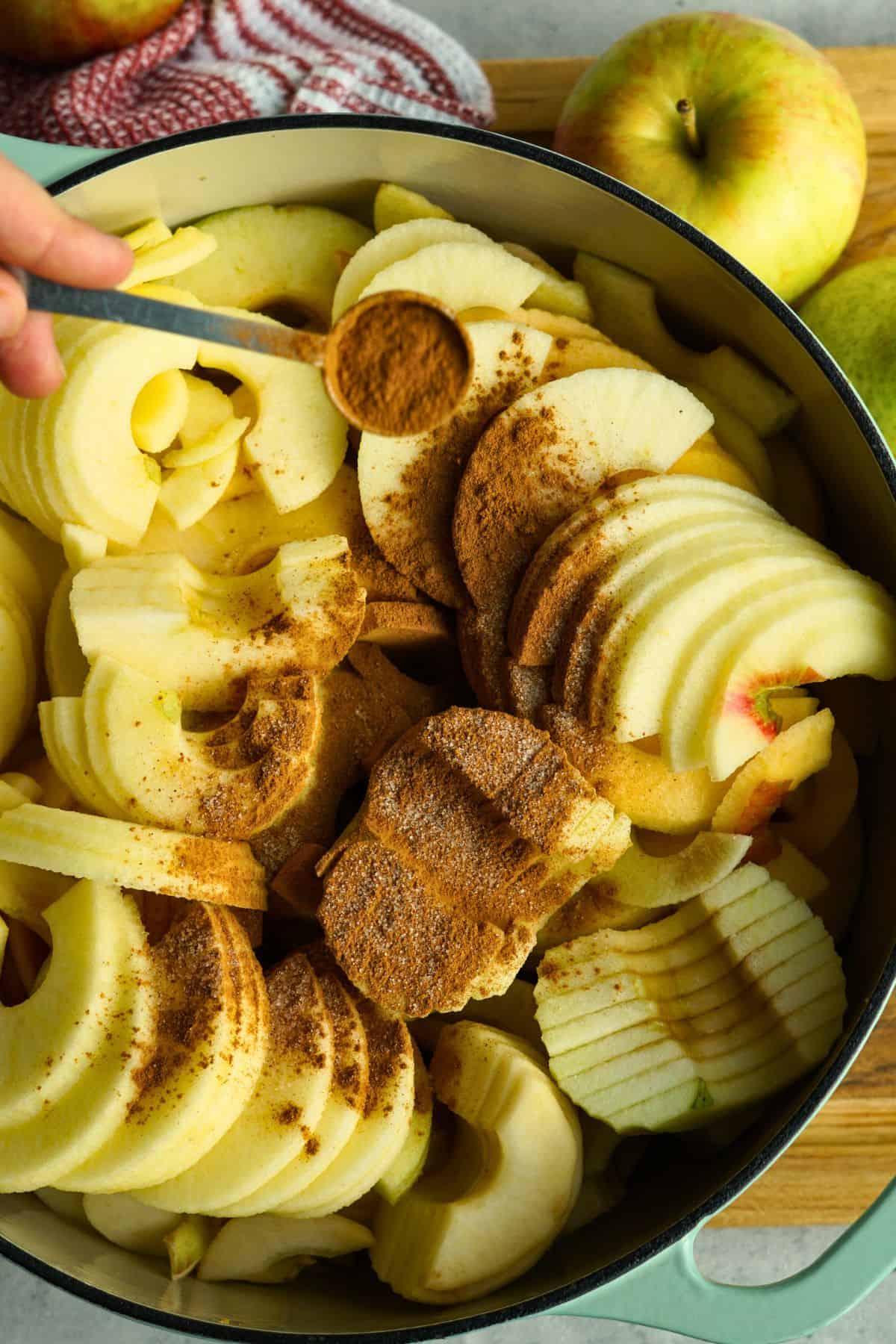 cinnamon being sprinkled over sliced apples in pot